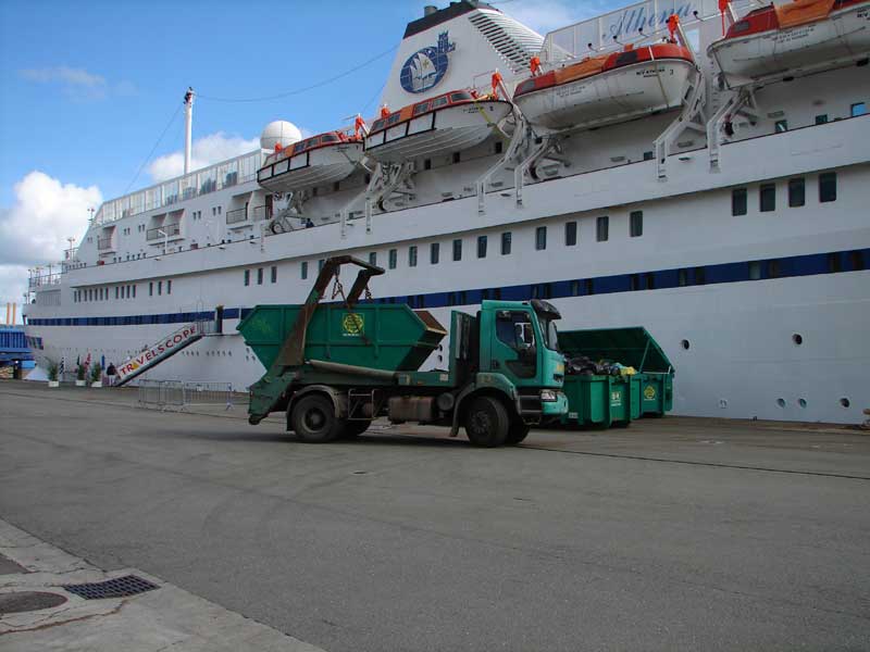 A skip-loader truck collecting solid waste beside the cruise ship Athena in Brest