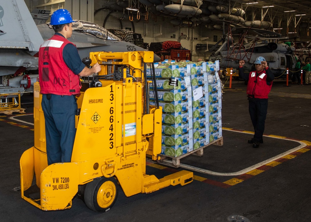 Sailors moving palletised lettuce boxes aboard USS George H.W. Bush during replenishment at sea