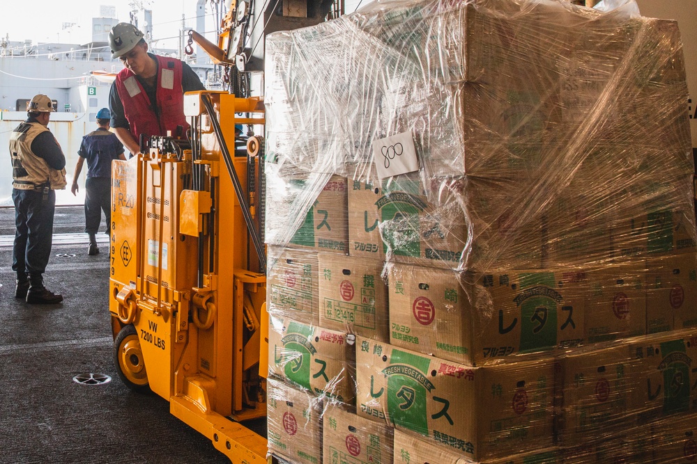 A forklift moving a wrapped pallet of fresh vegetable boxes inside USS Nimitz